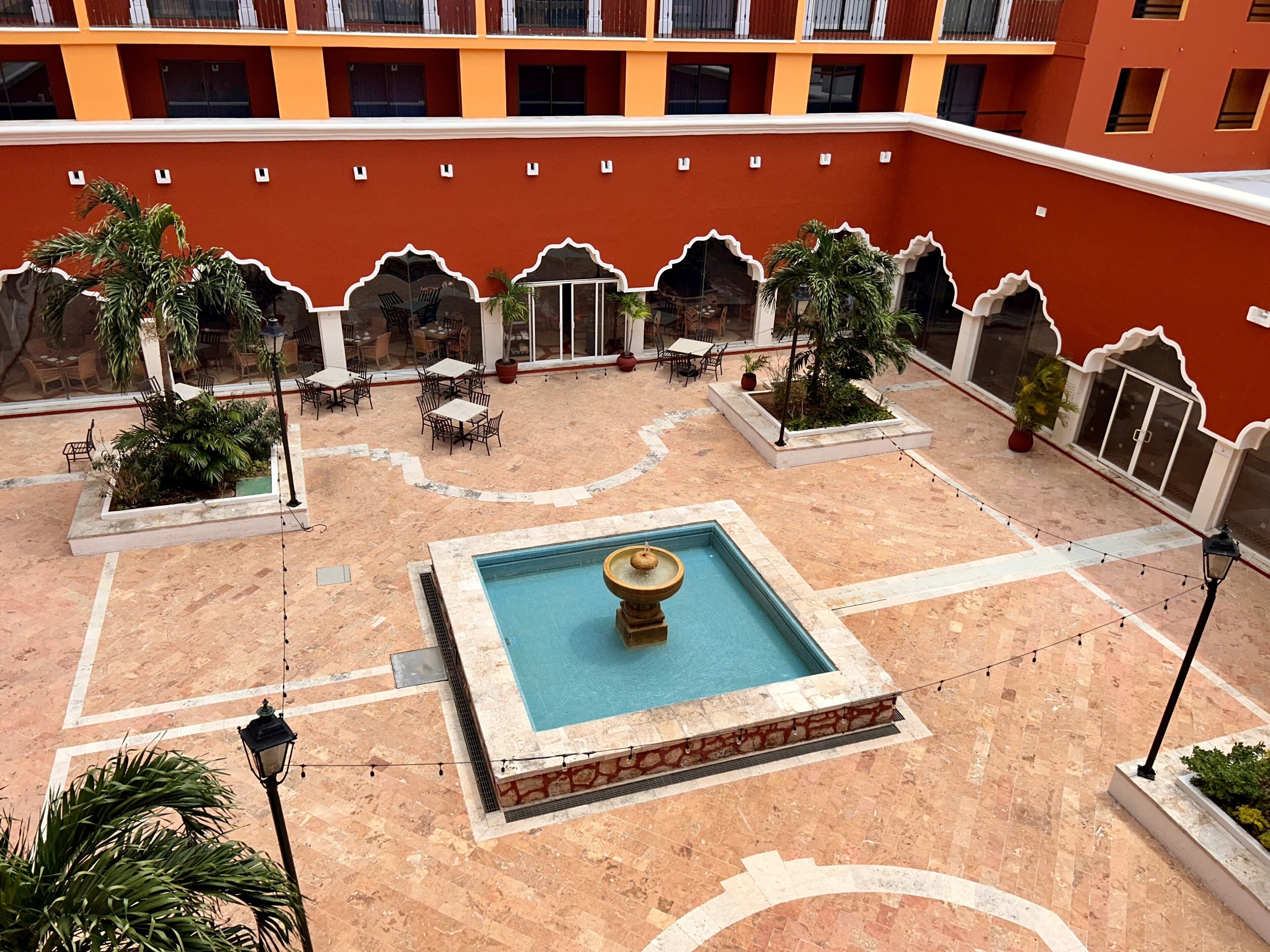 Une cour intérieure avec une piscine centrale, entourée d’espaces de détente en plein air et de plantes en pot.