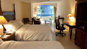 Habitación de hotel con dos camas, un escritorio, una silla y vista a la playa.