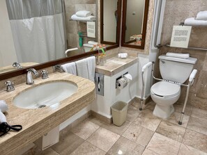 A bathroom with a sink, mirror, toilet, and handrails.