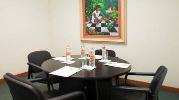 A conference room with a round table, four chairs, water bottles, and a framed painting on the wall.