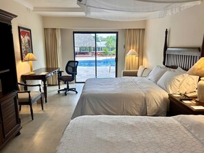 A hotel room with two beds, a desk, a chair, a TV, and a view of a swimming pool.