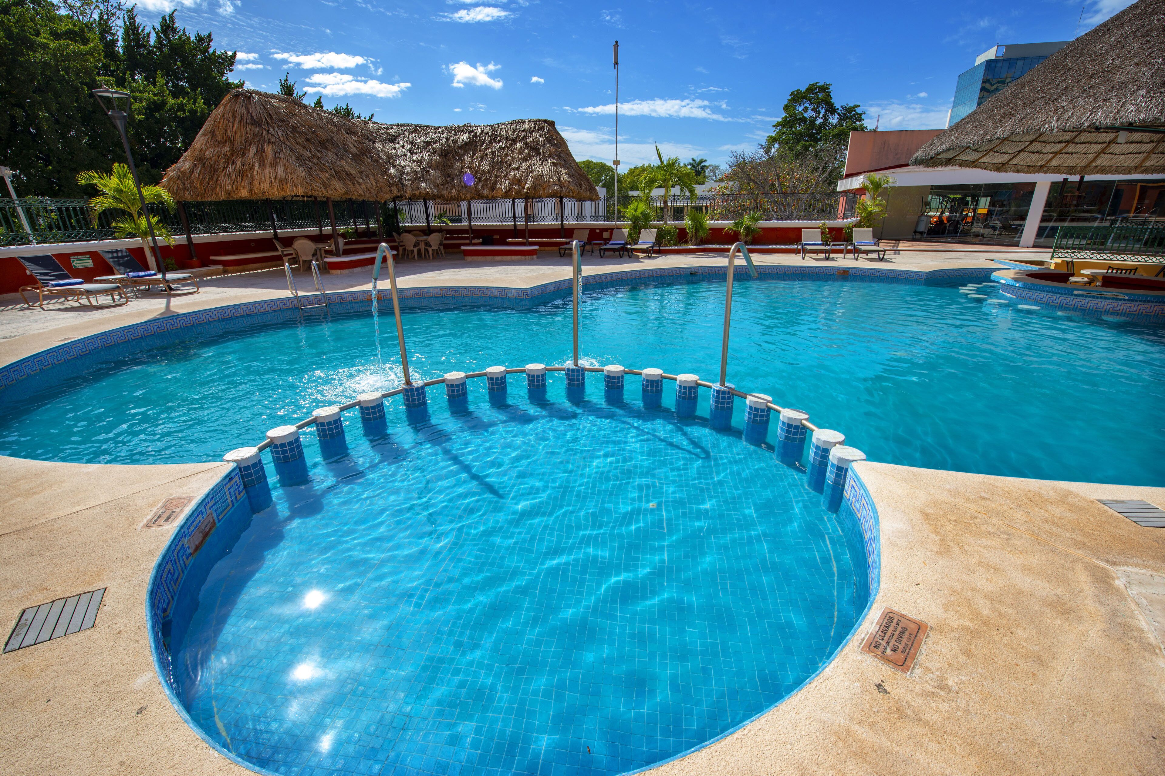 A swimming pool with a tiled edge, lounge chairs, and a thatched-roof structure in the background.