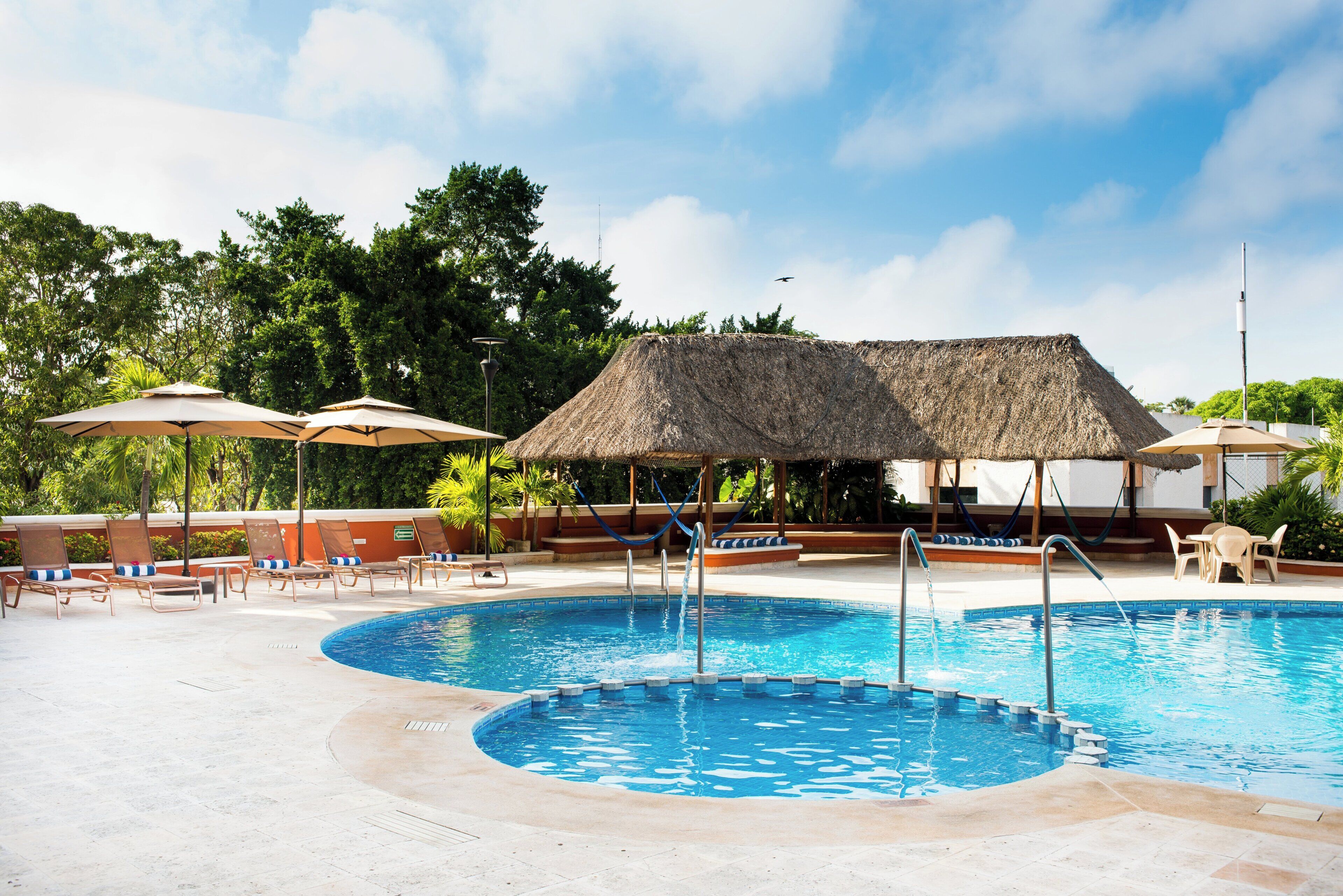 Un área de piscina con dos piscinas separadas, sillas de descanso, sombrillas y una estructura con techo de paja.