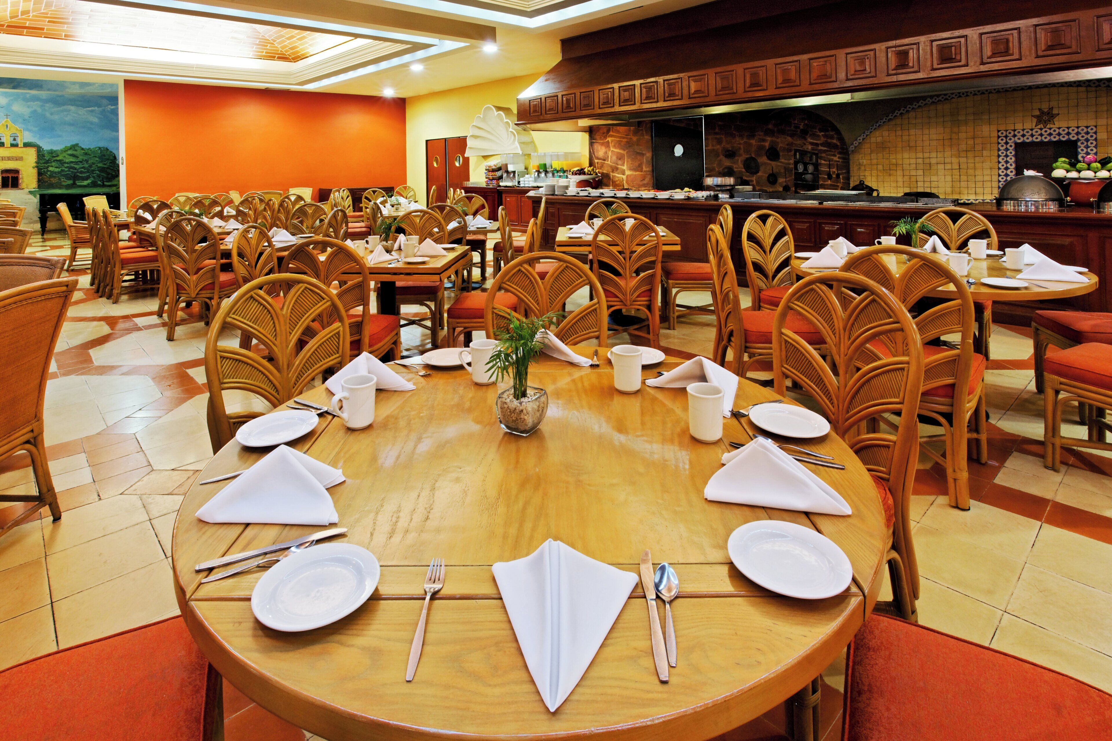 Un restaurante con varias mesas redondas preparadas para comer, con platos blancos, cubiertos y servilletas.