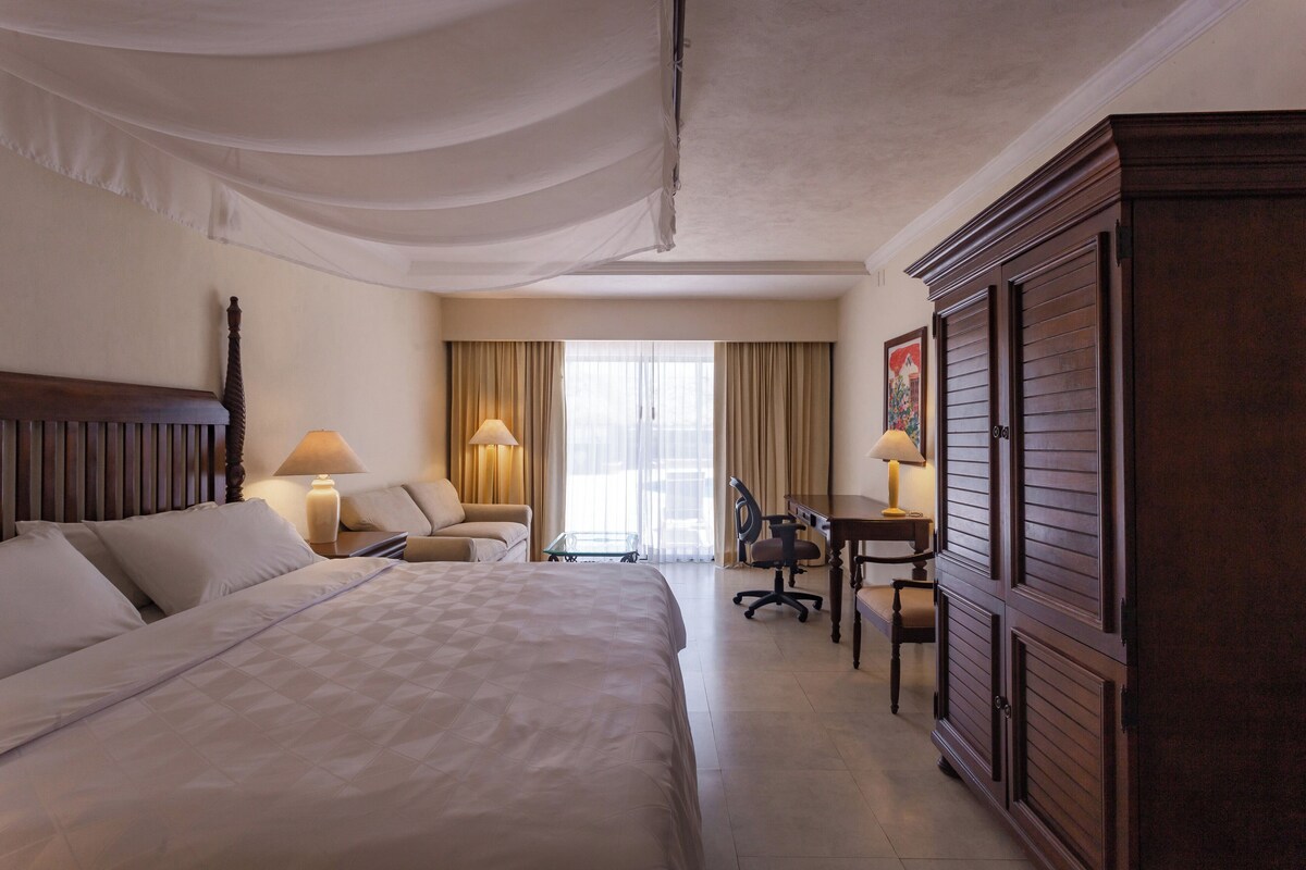 A hotel room with a large bed, a desk, a chair, and a wardrobe.