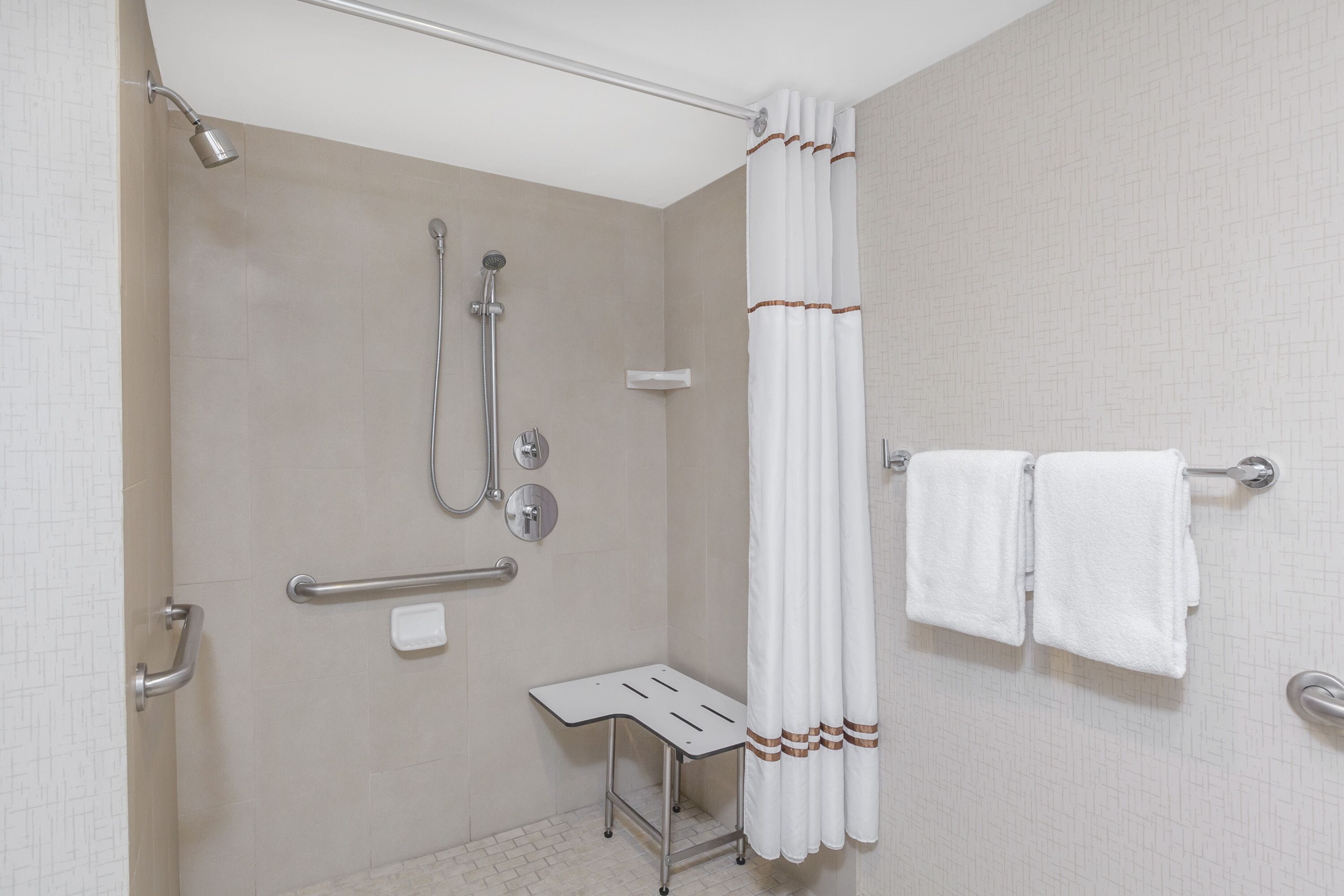 A modern bathroom with a shower, grab bars, a bench, and a towel rack.