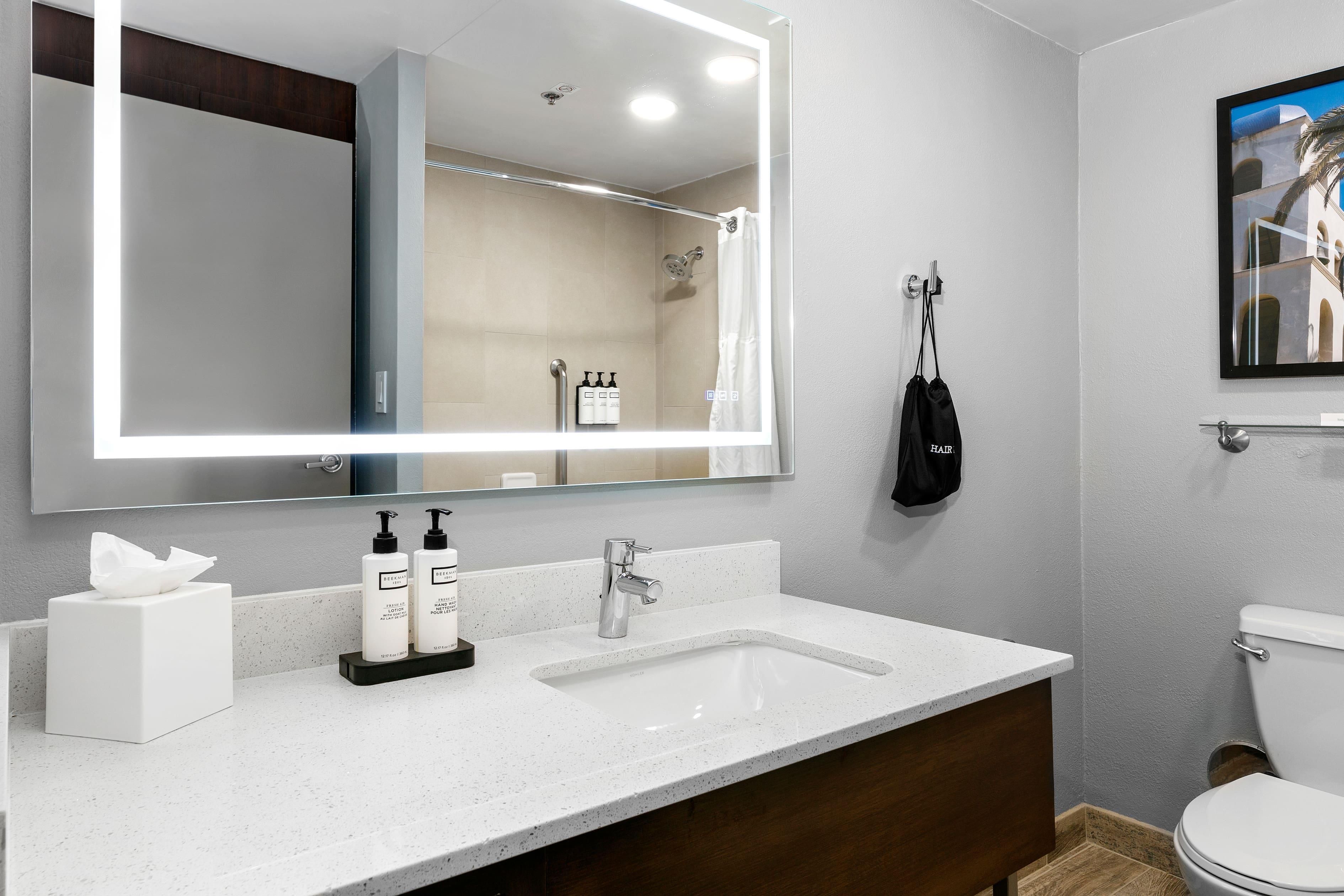 Une salle de bain moderne avec un grand miroir, deux lavabos, des toilettes et un tableau encadré au mur.