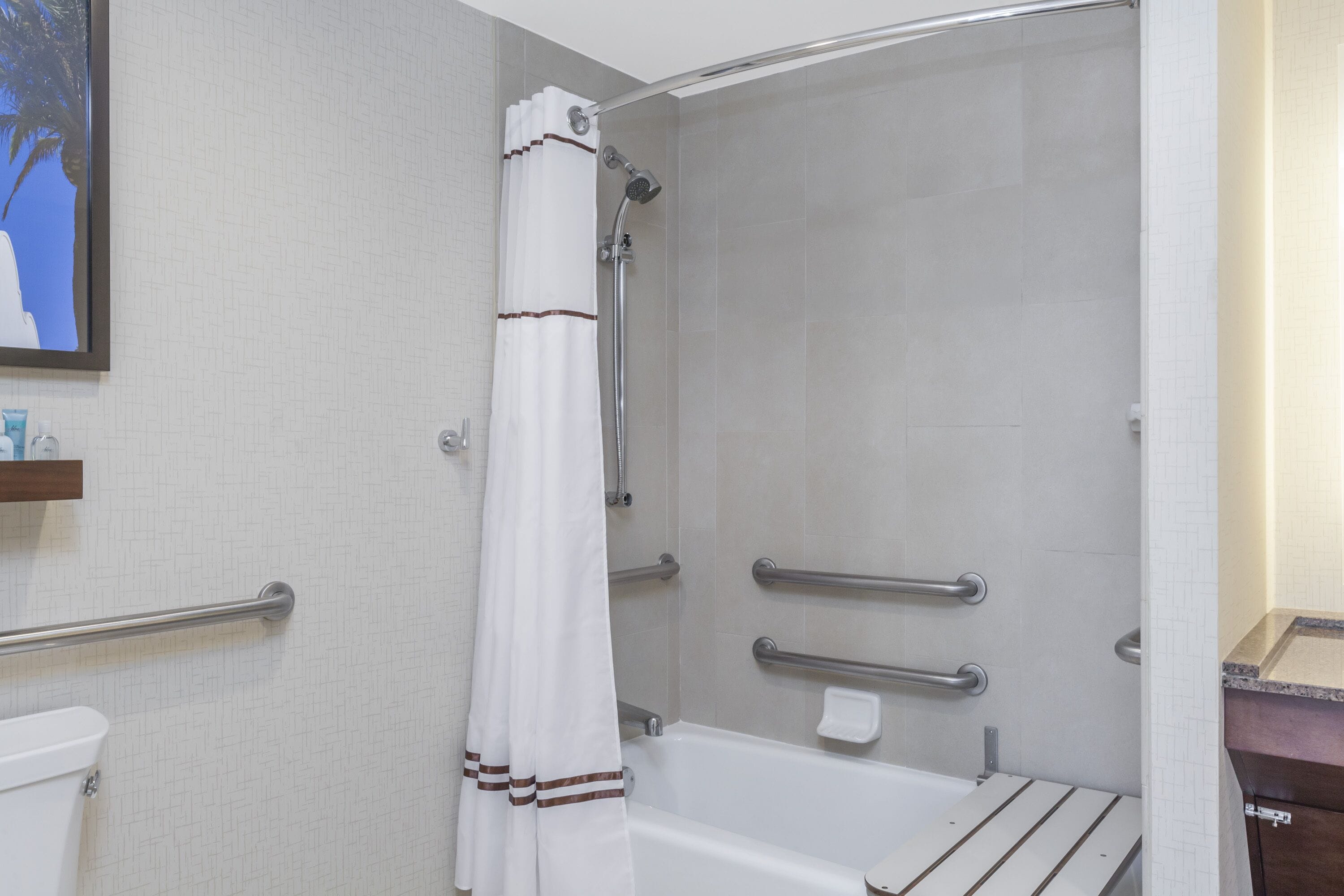 A bathroom with a shower, grab bars, a toilet, and a sink.