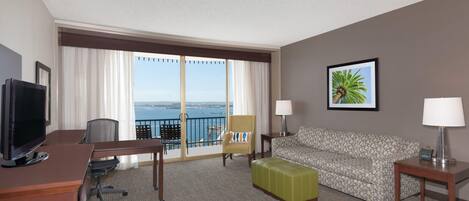 Habitación de hotel con escritorio, silla, sofá y vista al mar.