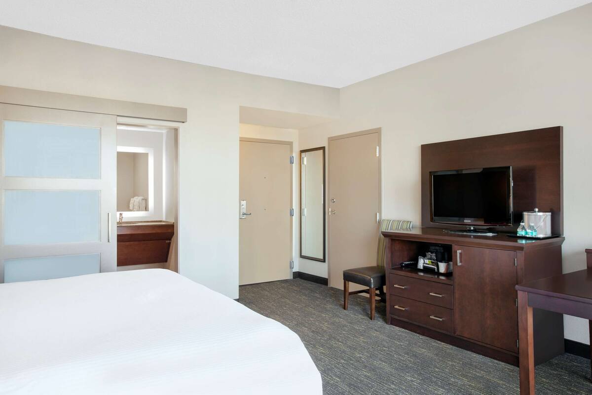 Een hotelkamer met een bed, een bureau met een televisie, een stoel en een kledingkast.