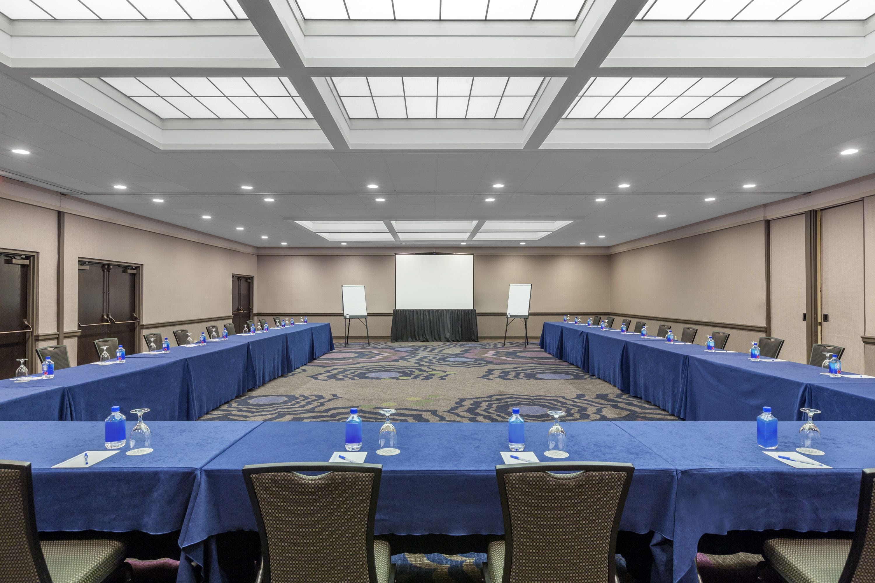 A conference room with a long table, chairs, water bottles, and a projector screen.