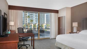 Une chambre d’hôtel avec un lit, un bureau, une chaise et une vue sur des immeubles de grande hauteur.