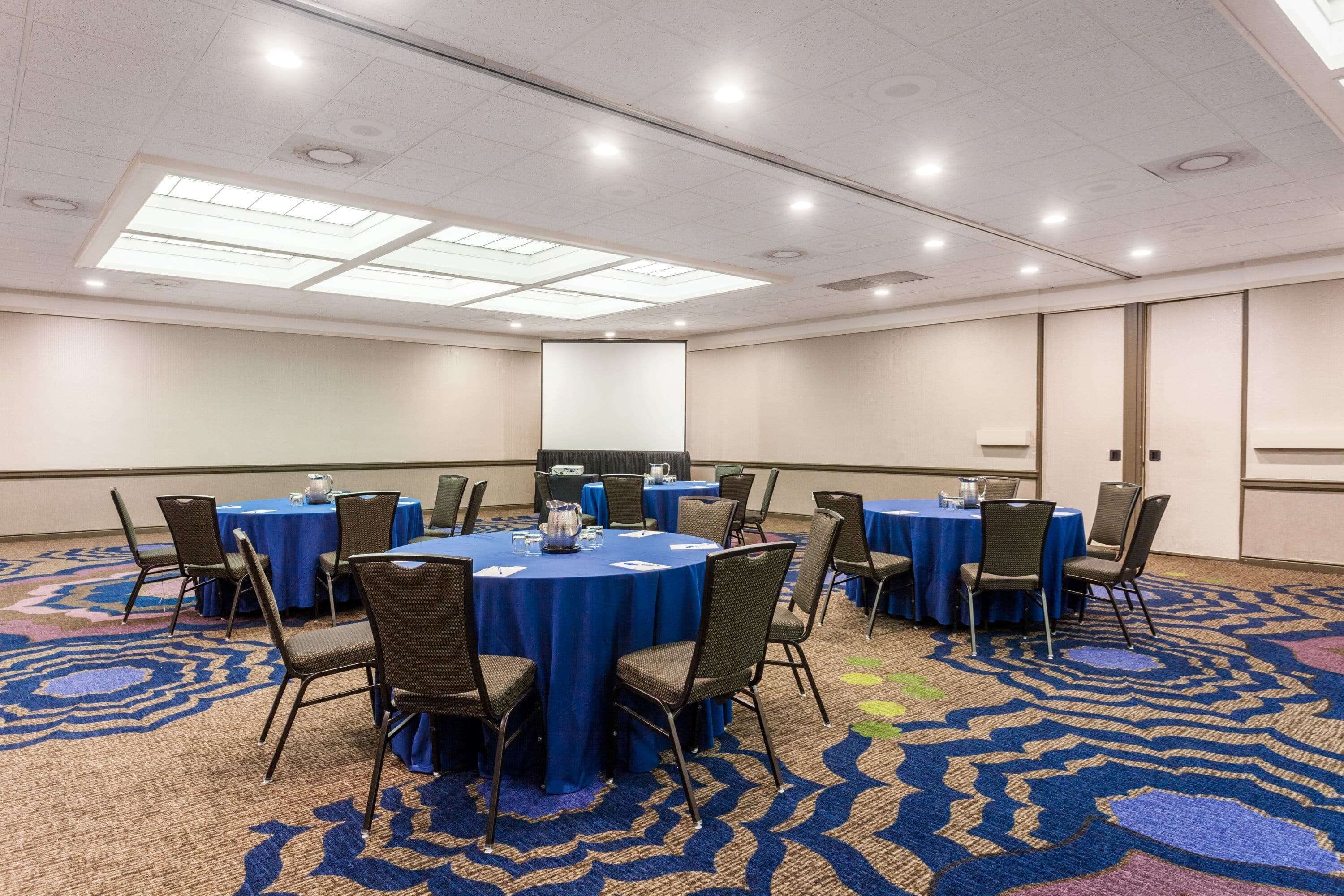 Une salle de conférence équipée de tables rondes, de chaises et d’un écran de projection.
