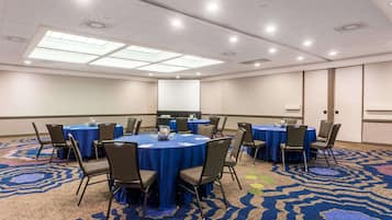 A conference room with round tables, chairs, and a projector screen.