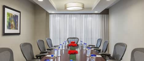 A conference room with a long table, chairs, water bottles, a vase with red roses, and a framed picture on the wall.