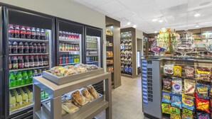 Un negozio di alimentari con banchi frigo per bevande, scaffali con snack e un'esposizione di prodotti confezionati.