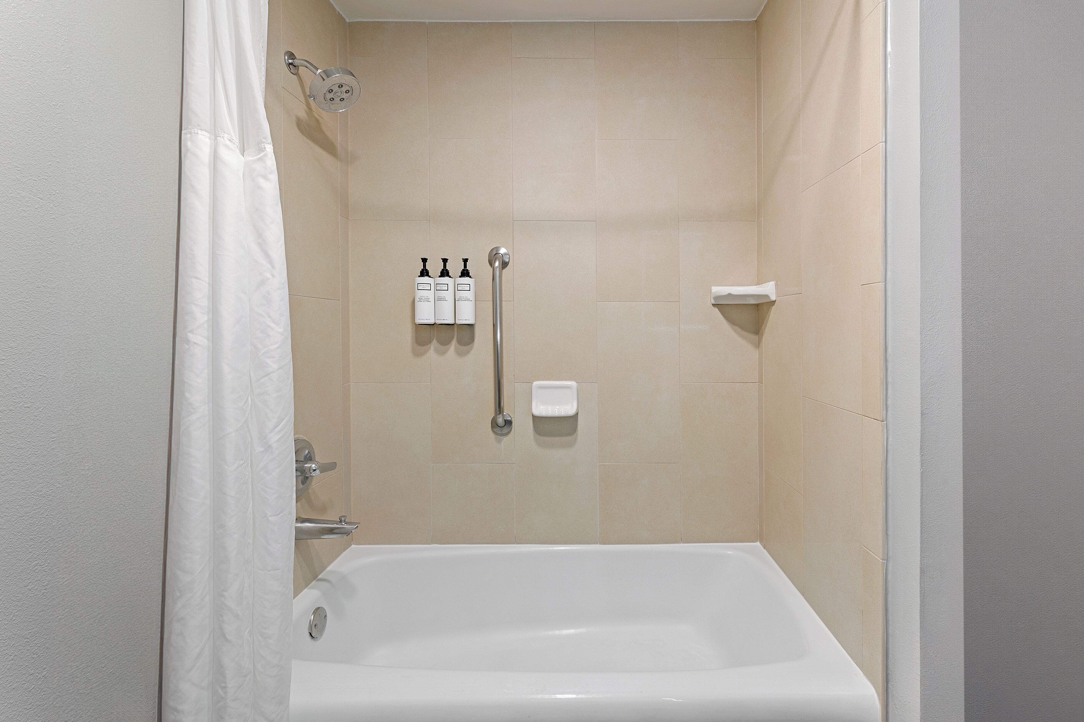 A modern bathroom with a bathtub, shower, and handrails.