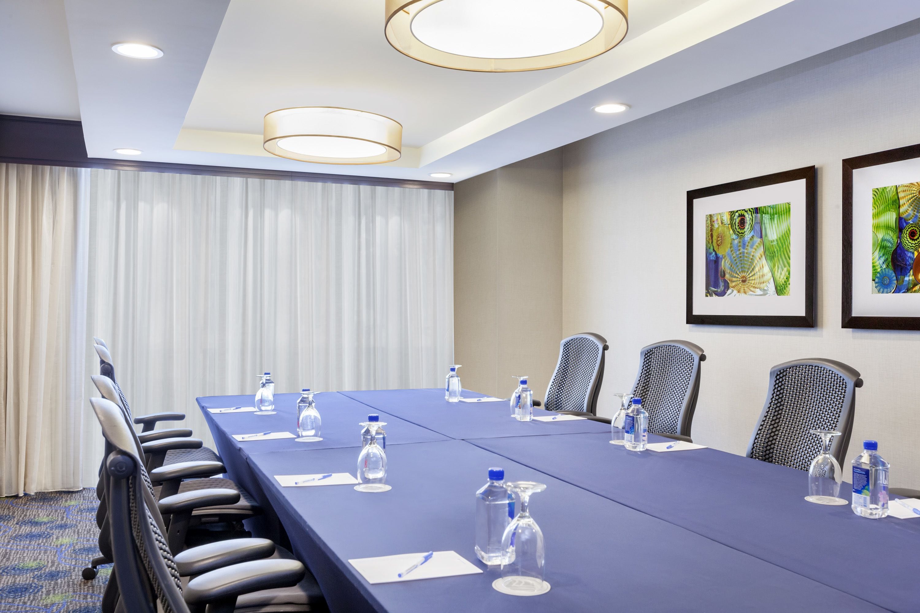 A conference room with a long table, chairs, water bottles, and framed artwork on the walls.