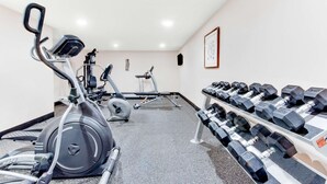Une salle de sport équipée de divers appareils, notamment un vélo elliptique, un vélo d’appartement et un porte-haltères avec des poids.