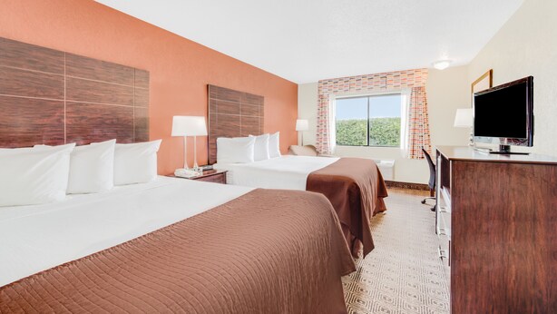 Une chambre d’hôtel avec deux lits, un bureau, une télévision et une fenêtre donnant sur un paysage verdoyant.