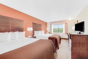 A hotel room with two beds, a desk, a television, and a window with a view of greenery.
