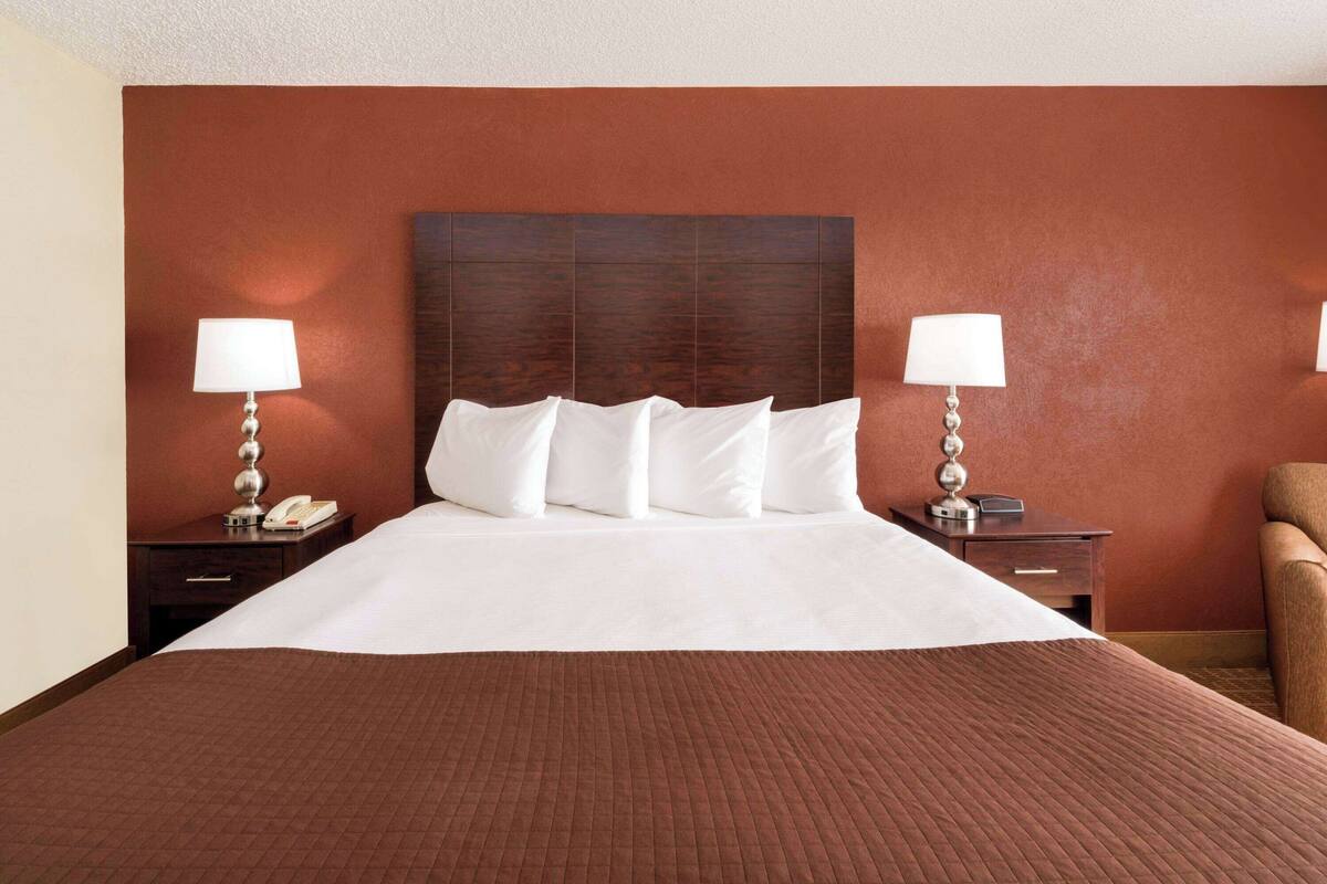 Une chambre d’hôtel avec un grand lit, deux tables de chevet avec des lampes, une tête de lit en bois et une moquette marron.