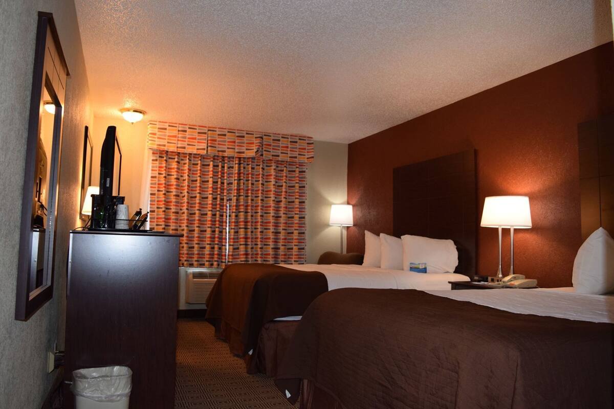 Une chambre d’hôtel avec deux lits, un bureau, une lampe et un rideau à motifs.