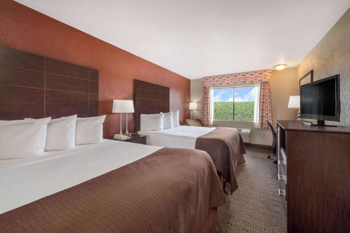 Une chambre d’hôtel avec deux lits, un bureau, une télévision et une fenêtre donnant sur un paysage verdoyant.