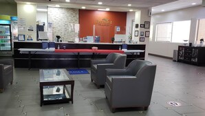 Un espace d’accueil comprenant un comptoir, des chaises, une petite table et un mur sur lequel est inscrit le nom de l’hôtel.