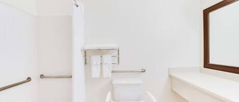 Un baño con inodoro blanco, ducha, barra de apoyo, taburete pequeño y un perchero para toallas.