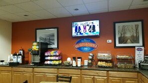 A breakfast counter with a television displaying a news program, a coffee machine, and various breakfast items.