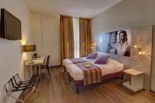 A modern hotel room with a large bed, a desk, a chair, and a TV mounted on the wall.