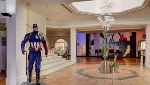 A statue of Captain America in a lobby with a staircase, a chandelier, and potted plants. - Hôtel Arles Plaza (Arles)