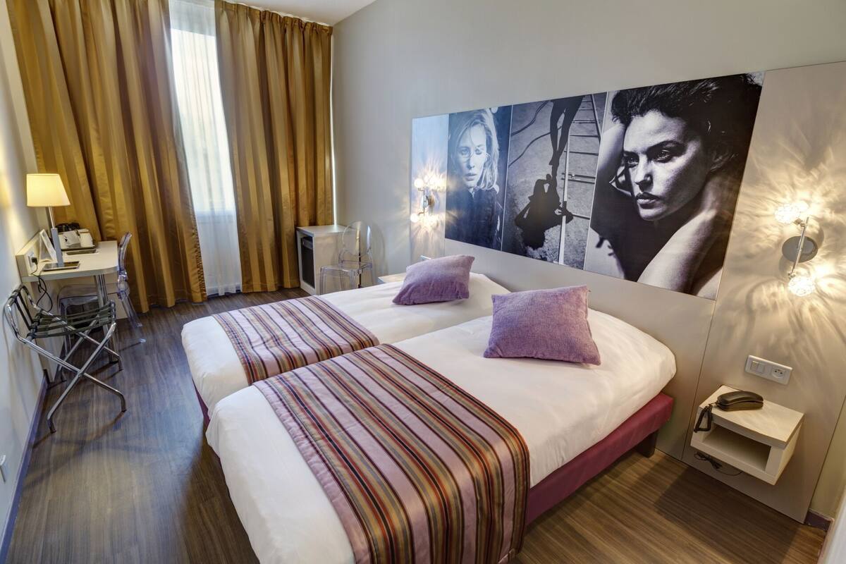 A hotel room with a large bed, two pillows, a desk with a lamp, and a chair.