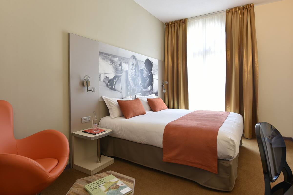 A hotel room with a bed, a chair, a small table, and a television.