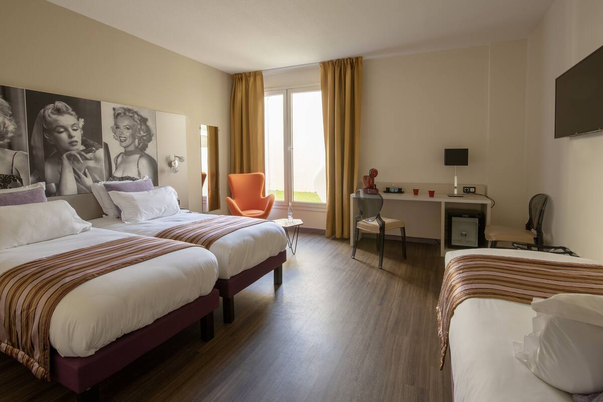 A hotel room with two beds, a desk, a chair, and a TV.