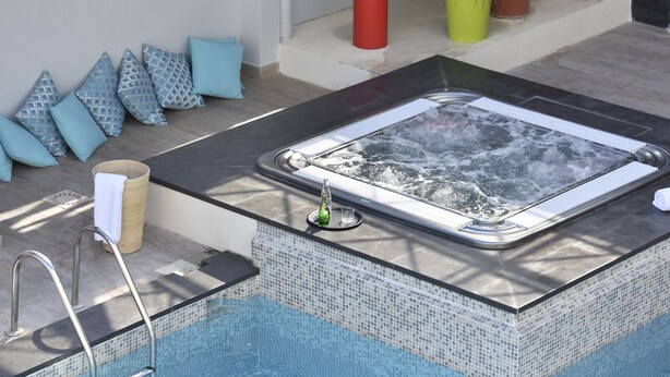 A hot tub with a tiled edge, a metal ladder, and a glass panel. - Hôtel Arles Plaza (Arles)