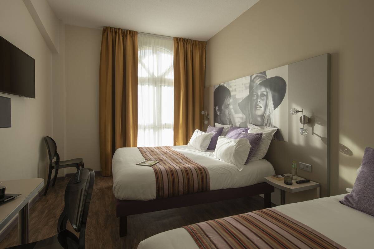A hotel room with a bed, a desk, a chair, a TV, and a window with curtains.