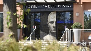 A hotel entrance with a large glass facade, a prominent sign reading "HOTEL ARLES PLAZA," and a staircase leading to the entrance. - Hôtel Arles Plaza (Arles)