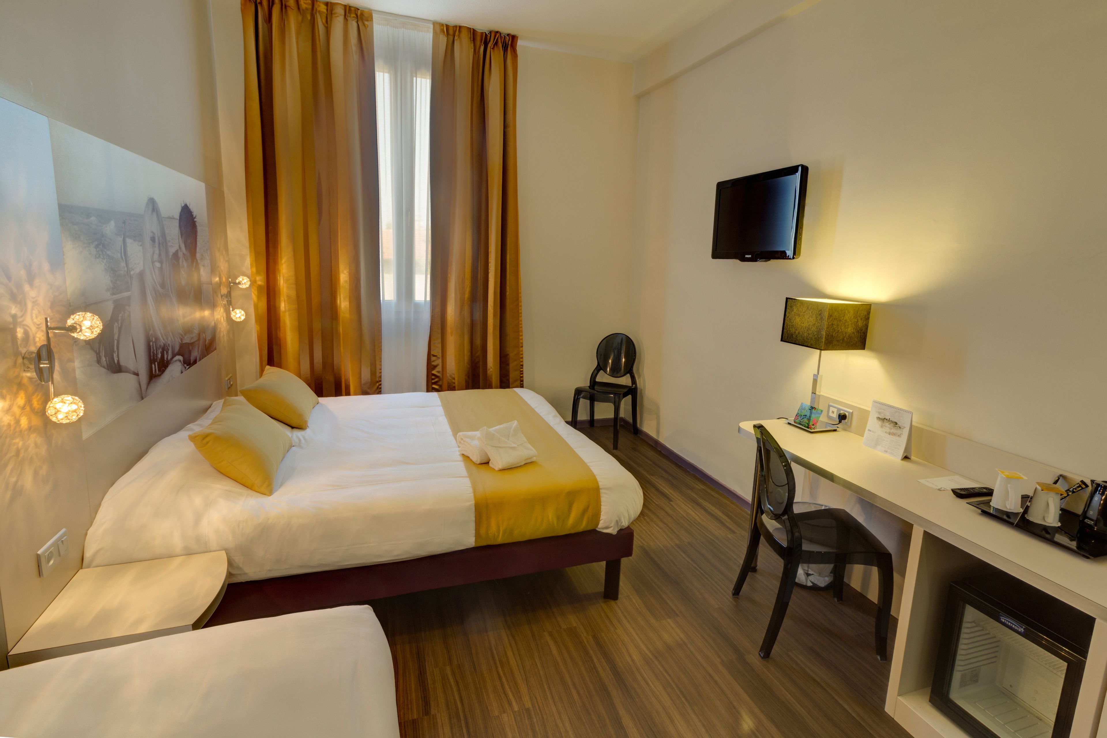A hotel room with a bed, a desk, a chair, a television, and a fireplace.