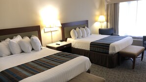 Une chambre d’hôtel avec deux lits, une banquette, une table de chevet et une lampe.