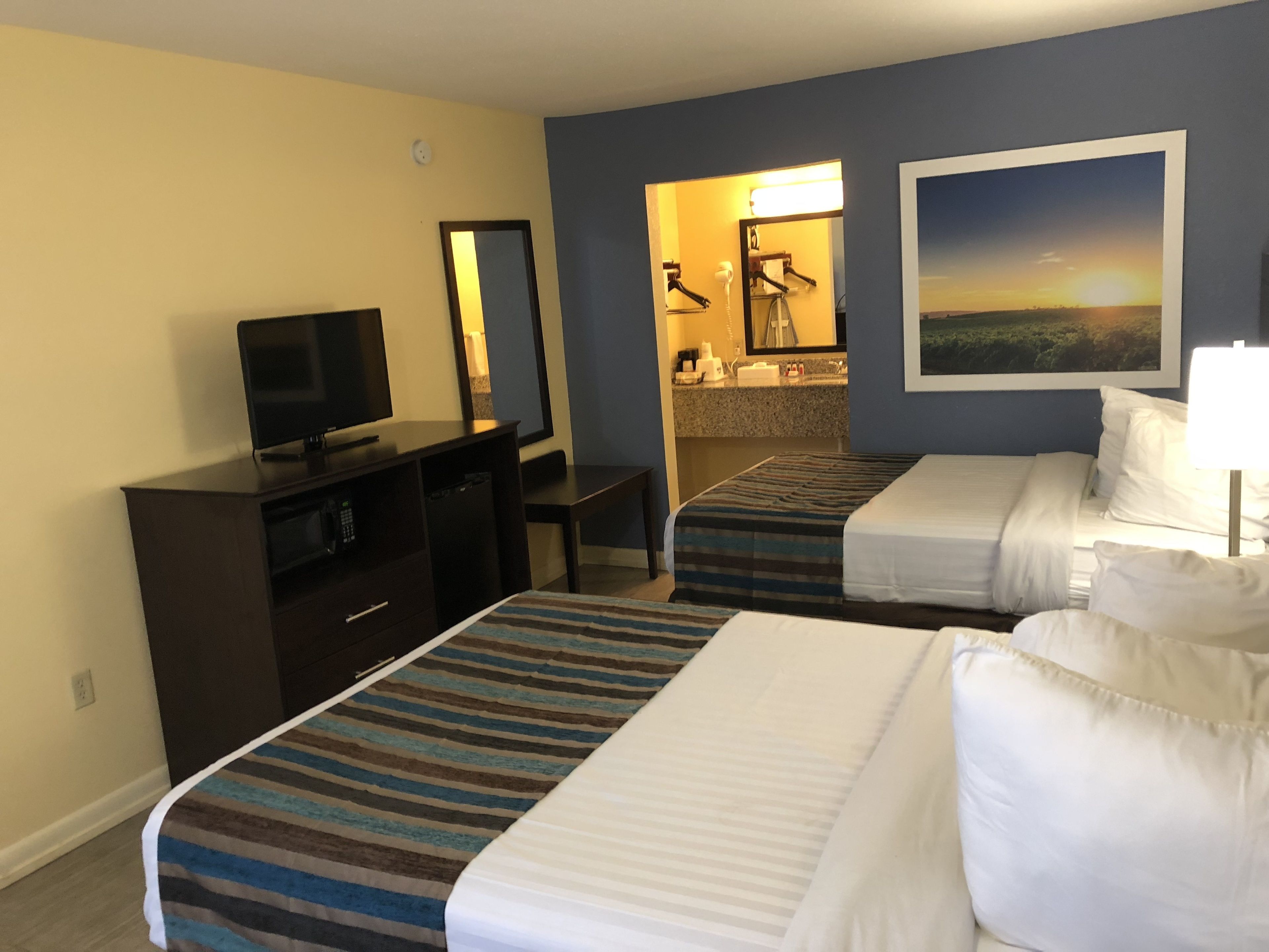 A hotel room with two beds, a TV, a desk, and a bathroom visible through an open door.
