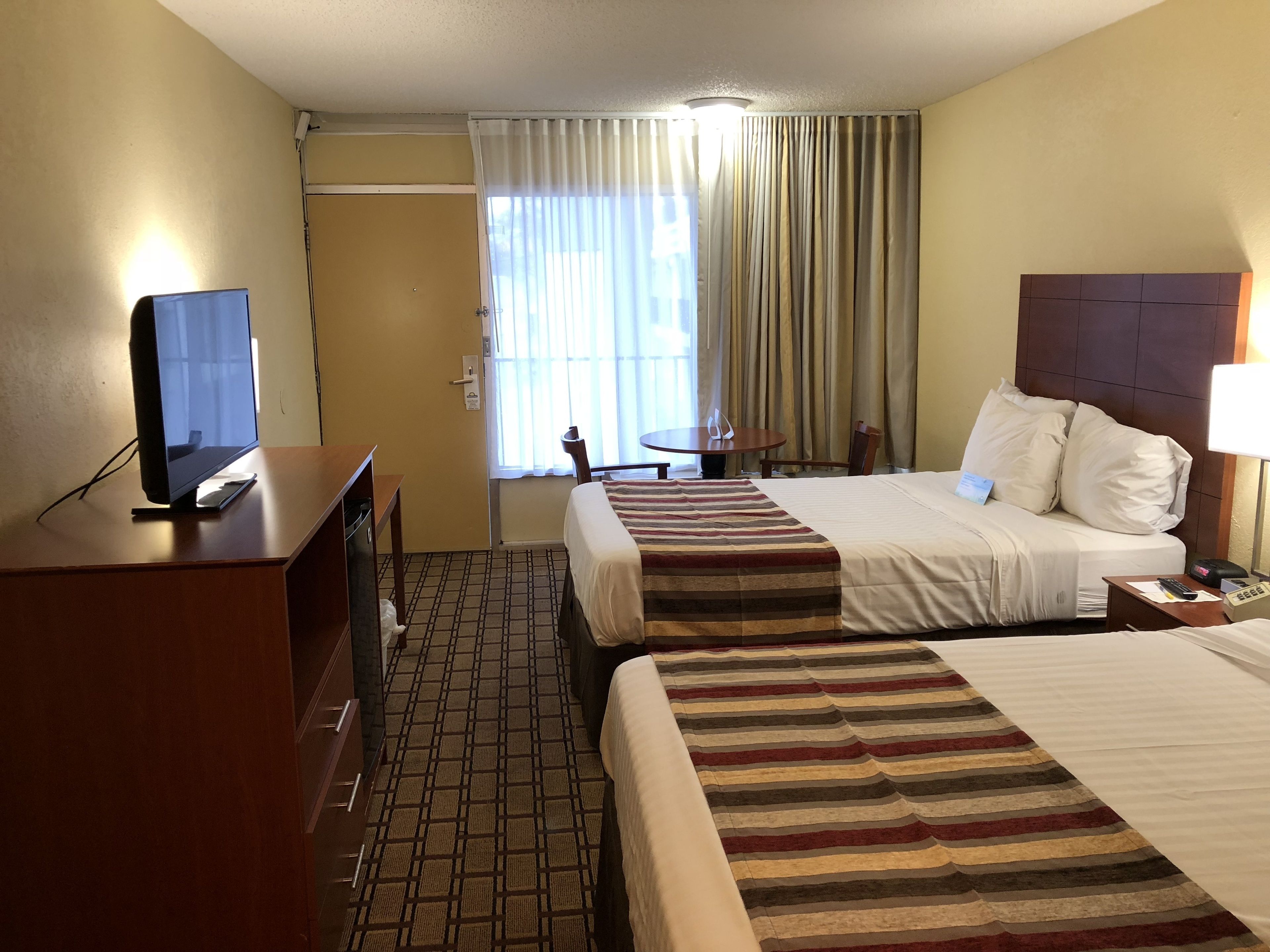 Habitación de hotel con dos camas, un escritorio con computadora, televisor y ventana con cortinas.