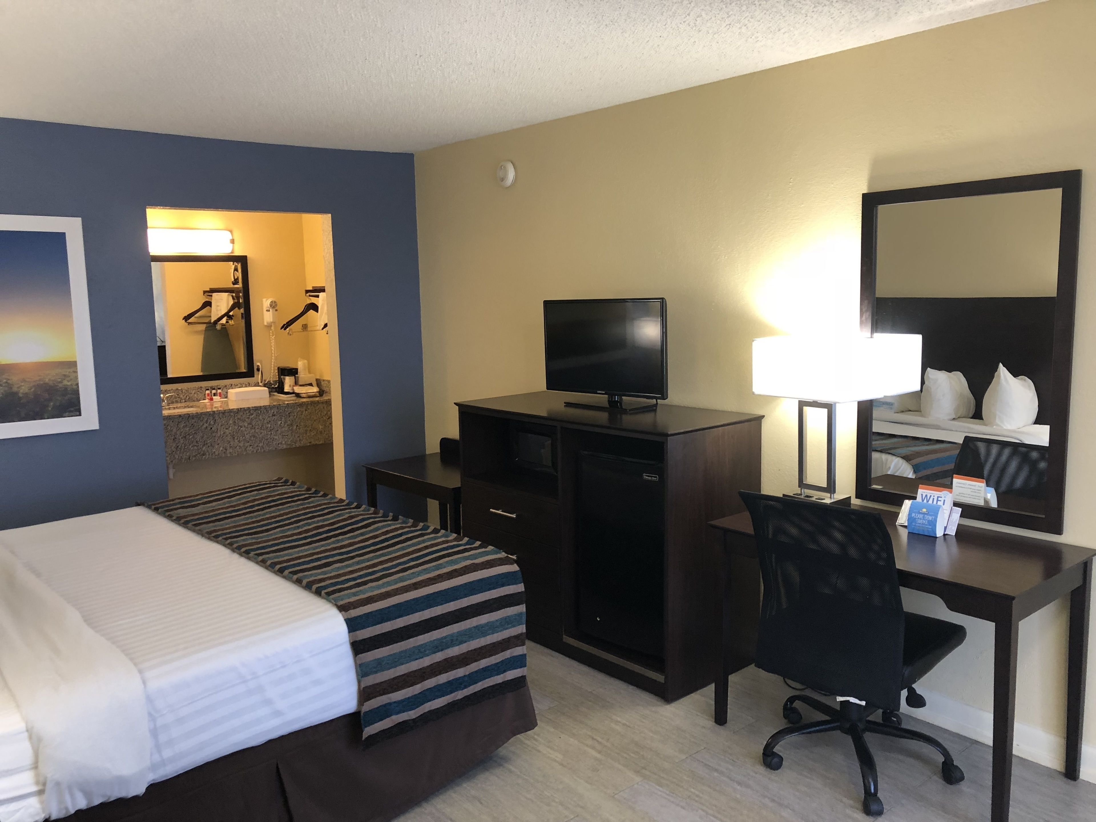 Une chambre d’hôtel avec deux lits, un bureau, un ordinateur, une télévision, une lampe et un miroir.