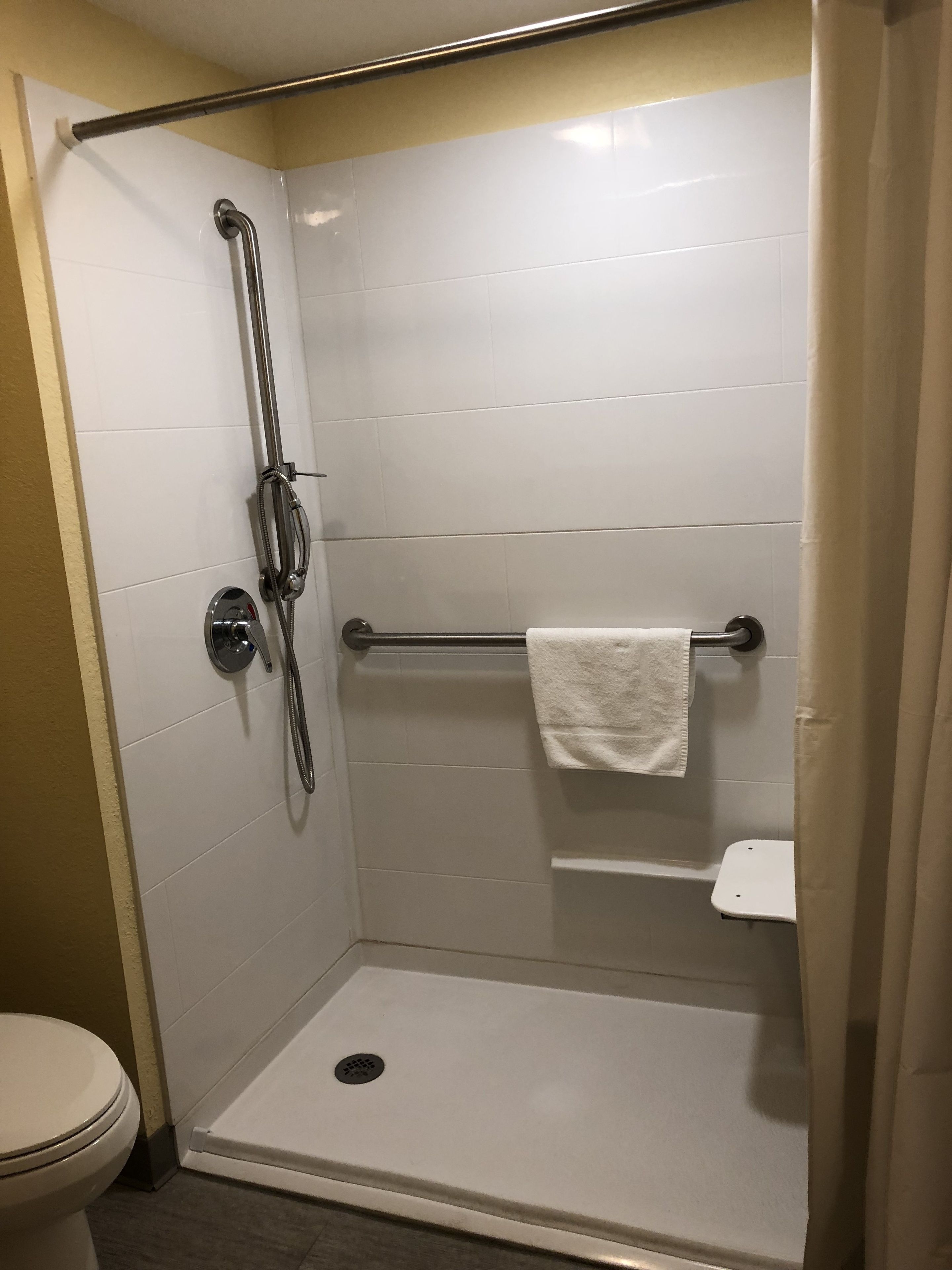 A small, enclosed shower stall with a grab bar, a towel rack, and a toilet.