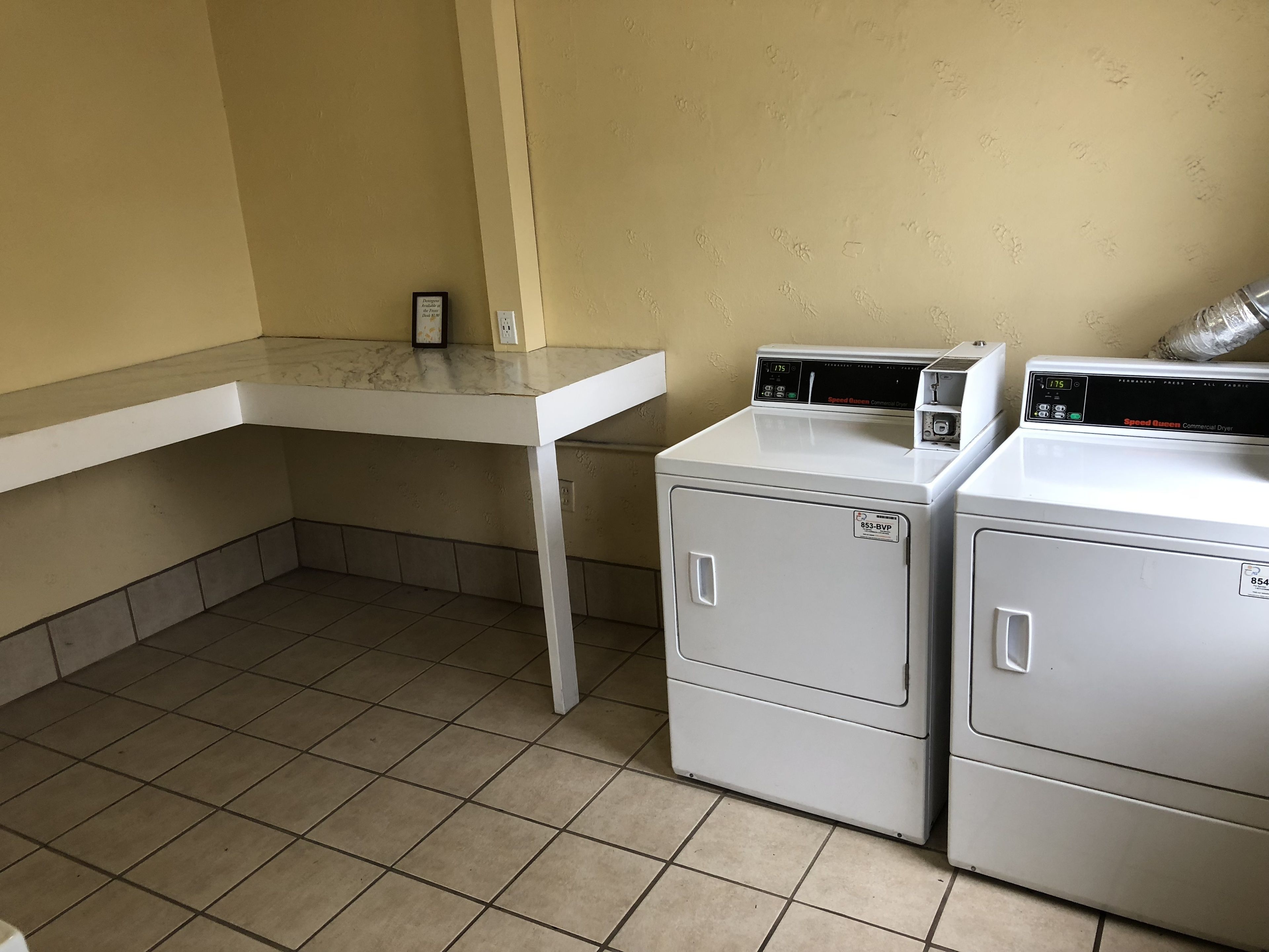Una sala de lavandería con dos lavadoras blancas de carga frontal y una mesa blanca.