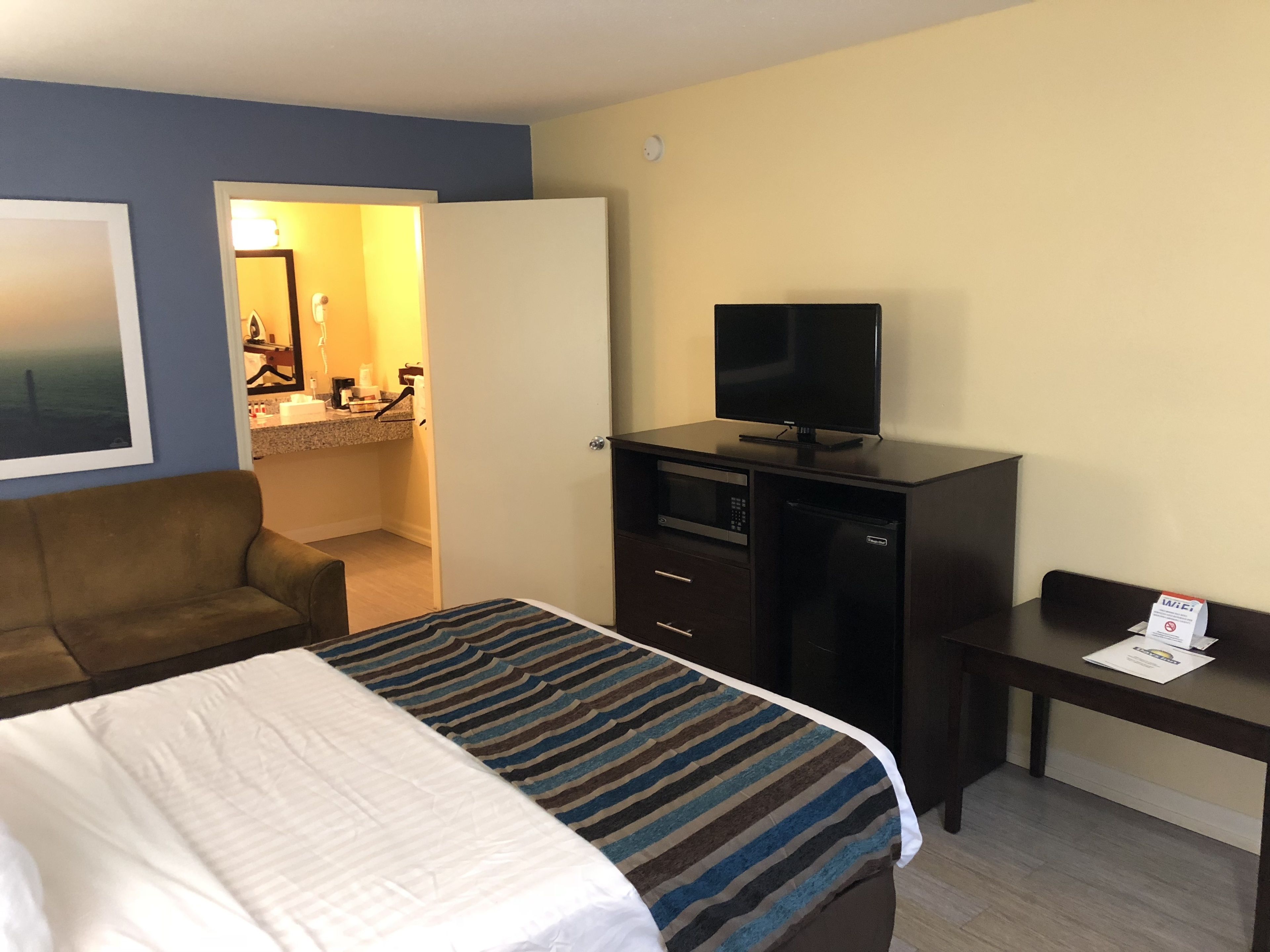 Une chambre d’hôtel avec un lit, un bureau, une télévision et une salle de bain visible à travers une porte ouverte.
