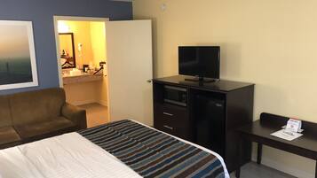 Une chambre d’hôtel avec un lit, un bureau, une télévision et une salle de bain visible à travers une porte ouverte.