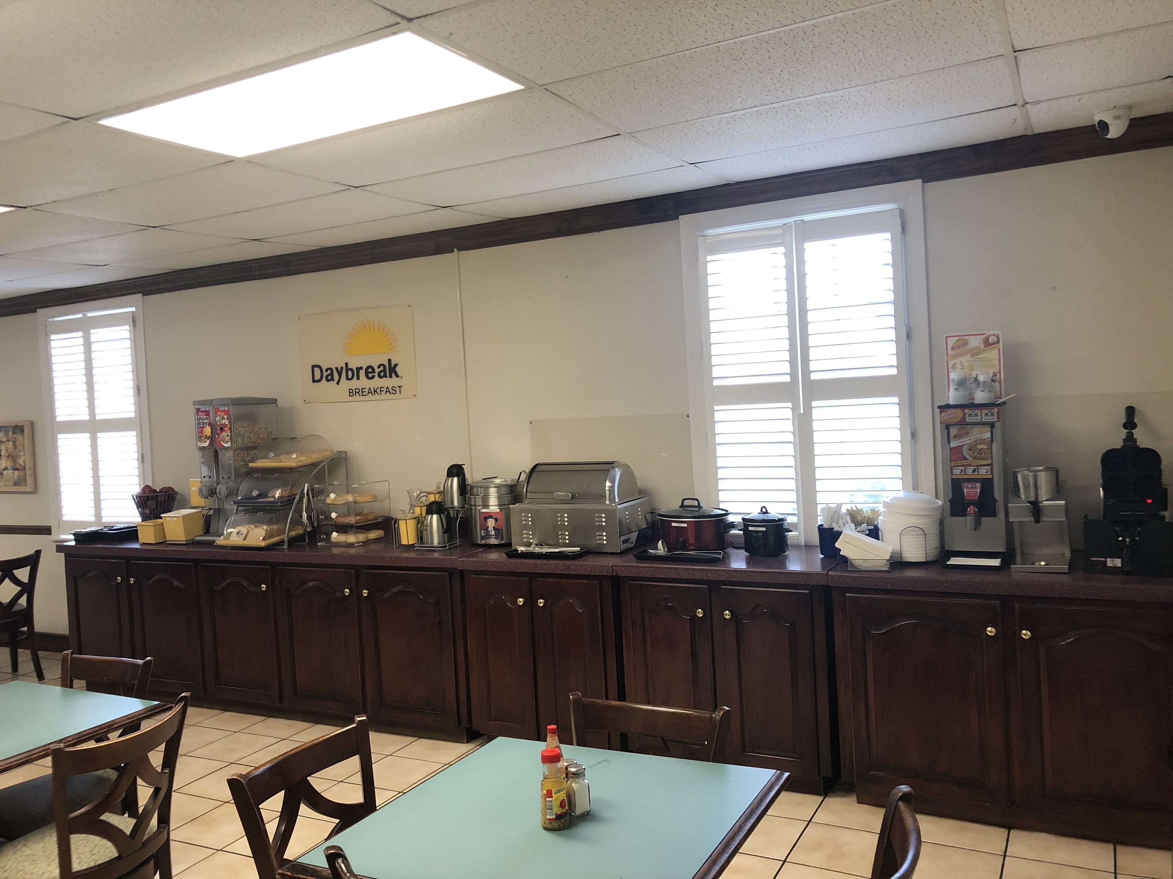 Espaço de café da manhã com um letreiro indicando "Daybreak Breakfast", equipado com máquinas de café, torradeira e diversos itens alimentares.
