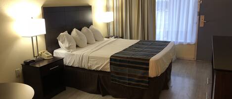 Habitación de hotel con una cama, lámparas de noche, un escritorio con teléfono, una silla y una ventana con cortinas.